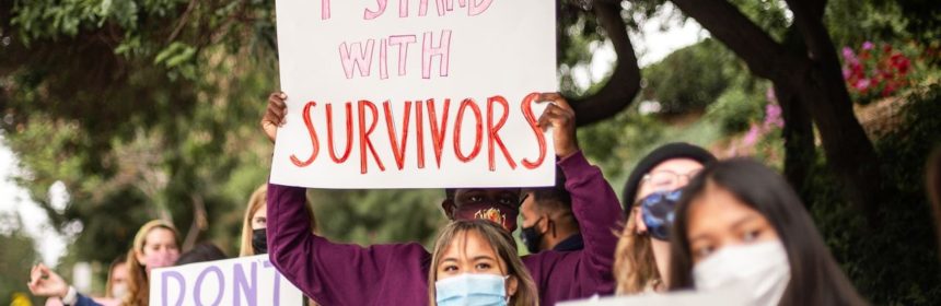 Students hold poster reading "I Stand with Survivors"