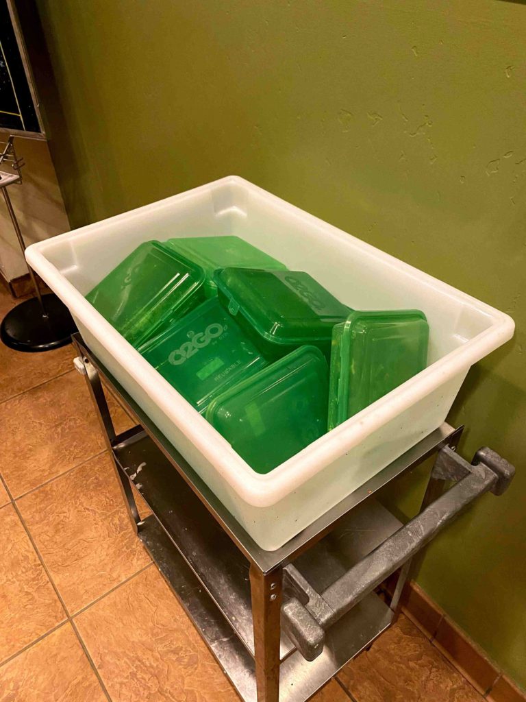 Large white bin holding smaller green to-go containers
