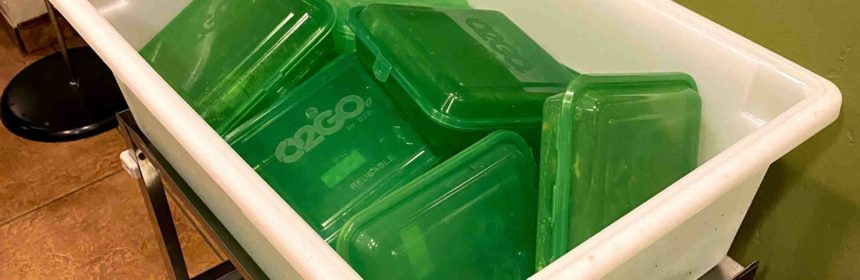 Large white bin holding smaller green to-go containers