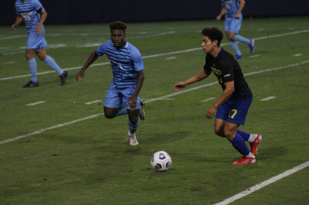 Two soccer players from opposing teams running towards the ball