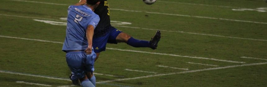 Action shot of men's soccer game after one player kicks the ball into the air