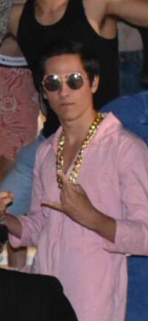 Male wearing sunglasses and pink collared shirt posing for photograph