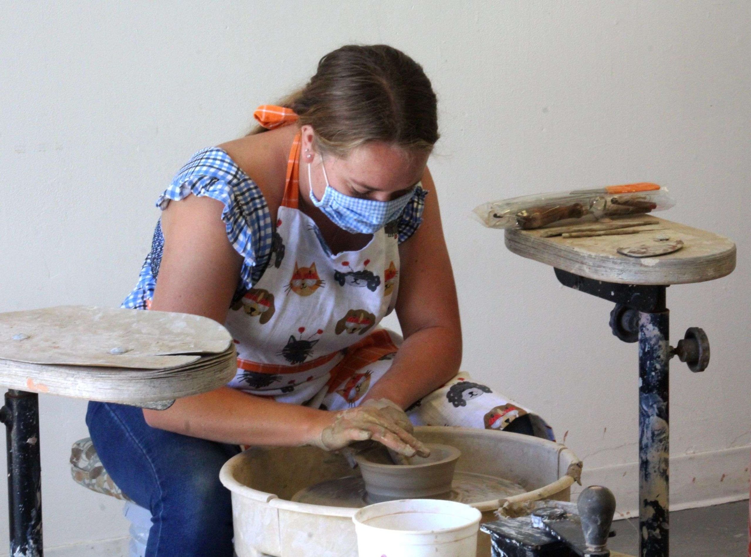 Student leaning over a pottery wheel making a pot