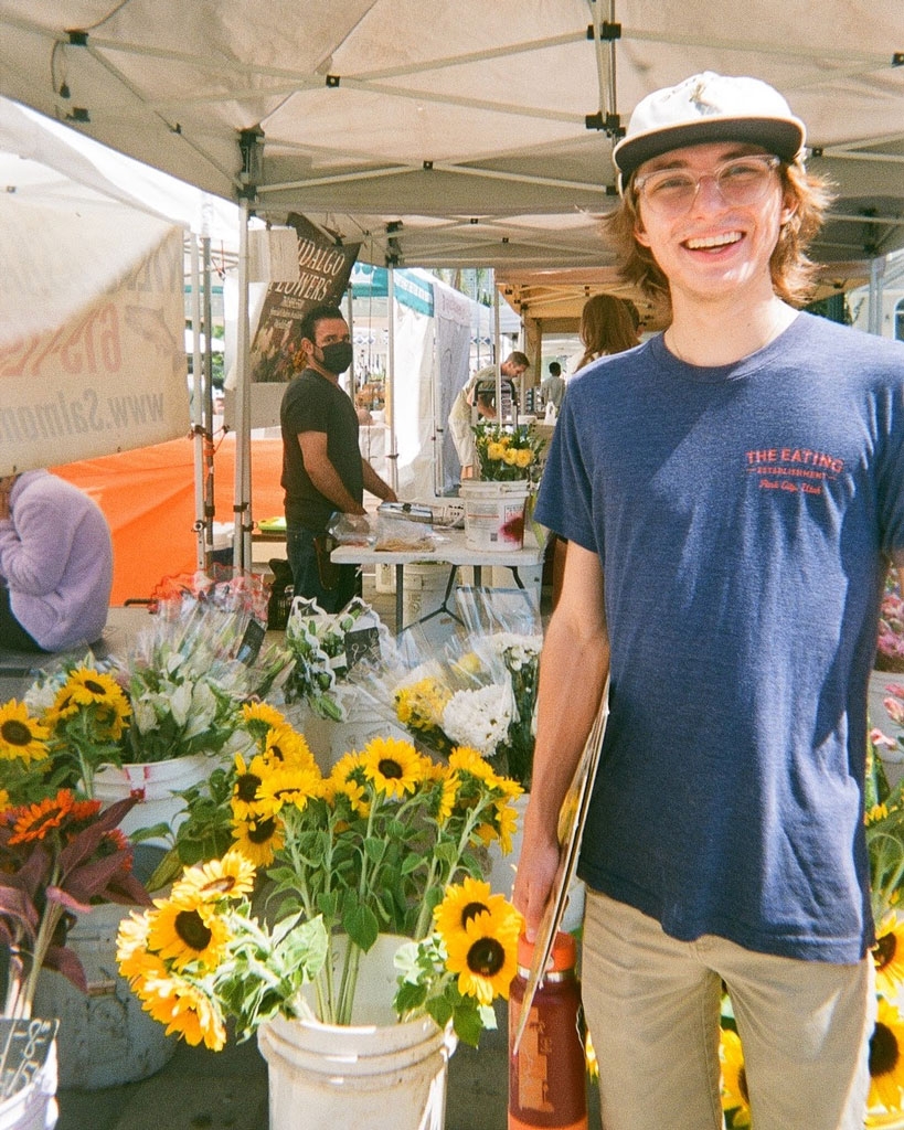 Male student standing in front of sunflower booth at farmers market