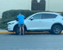 Man wearing blue uniform shirt putting a parking ticket on white SUV