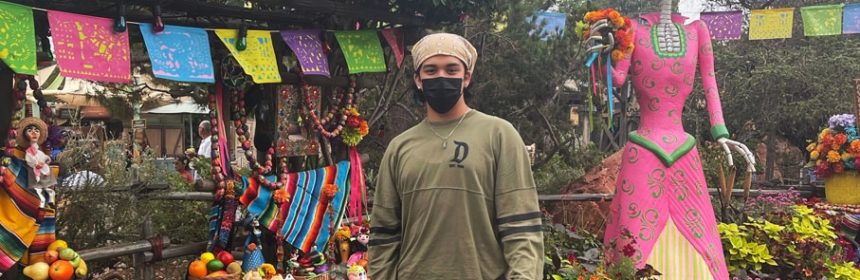Male student standing in front of colorful plants and hanging Papel Picado