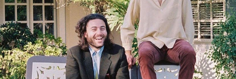 Two men sitting outside on a bench dressed stylistically