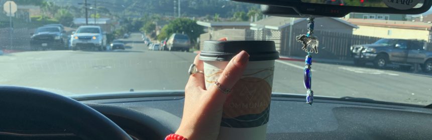 Hand holding coffee mug up in front of car window