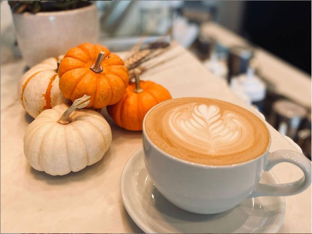 Latte with decorative foam art on table with tiny pumpkins