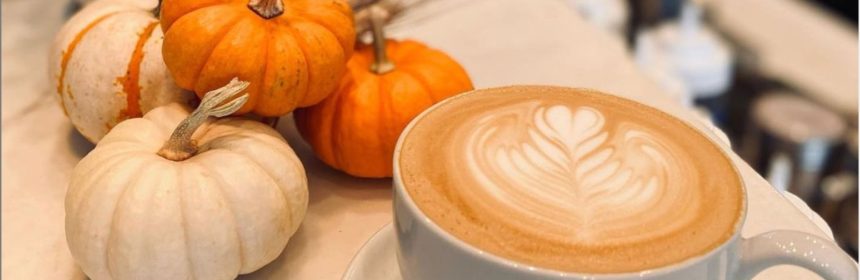 Latte with decorative foam art on table with tiny pumpkins