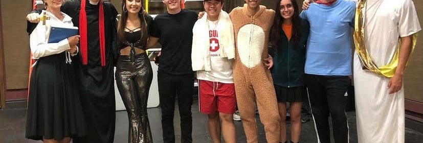 Group of students in an assortment of costumes standing on a stage