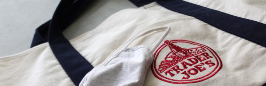 Canvas tote bag with red embroidered Trader Joe's logo and white face mask