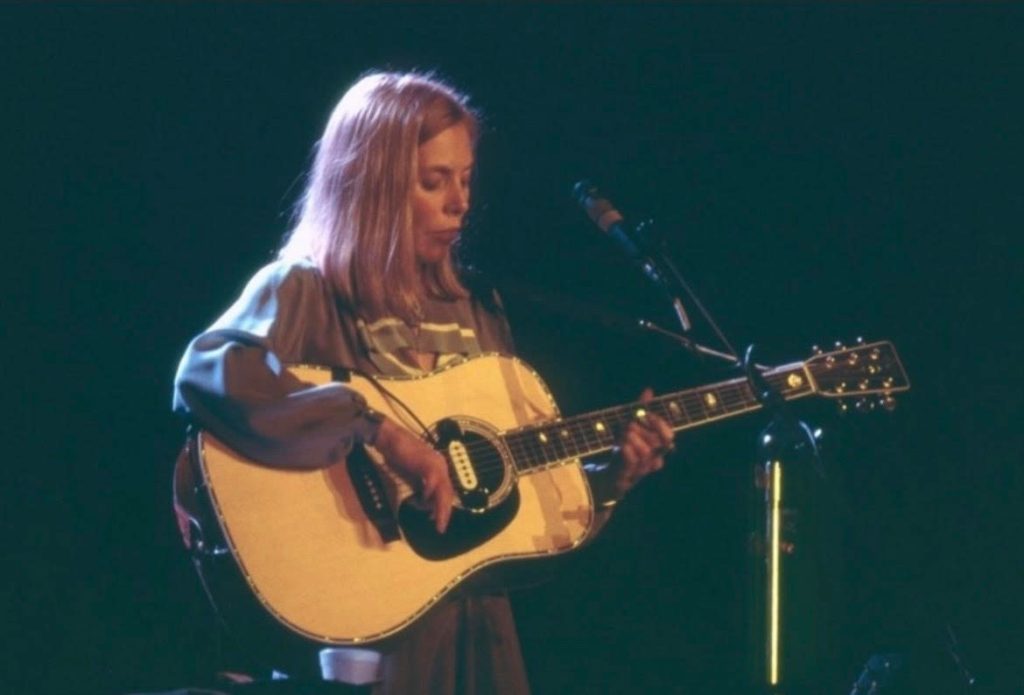 Joni Mitchell performing on stage with a guitar in arms