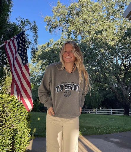 girl smiling outside with trees in the back wearing a USD sweatshirt