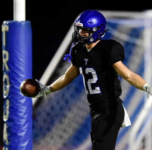 boy wearing football helmet in a black uniform with the number 12 celebrating on the field