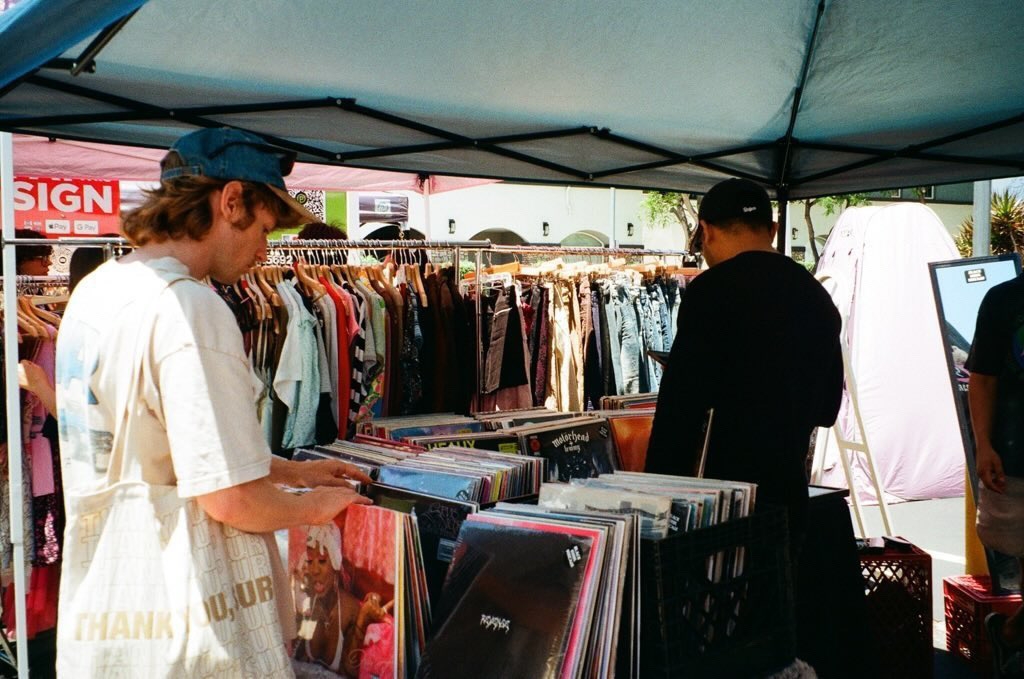two men in hats under a tent looking through racks full of clothes