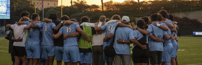 soccer players on field in a huddle with the sun setting in the back