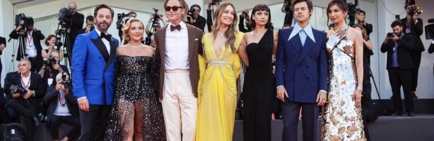 seven people lined up on the red carpet wearing suits and dresses smiling for paparazzi