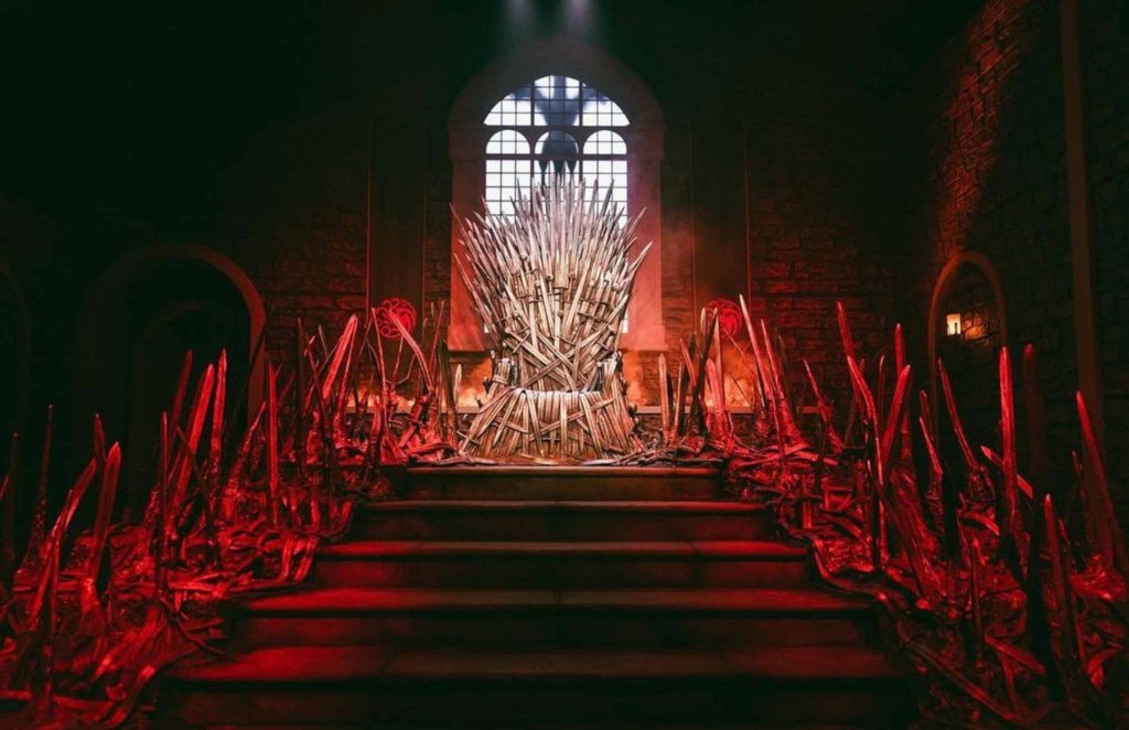 darkly lit stairs with throne in middle with red lights leading up to it and tall window behind it