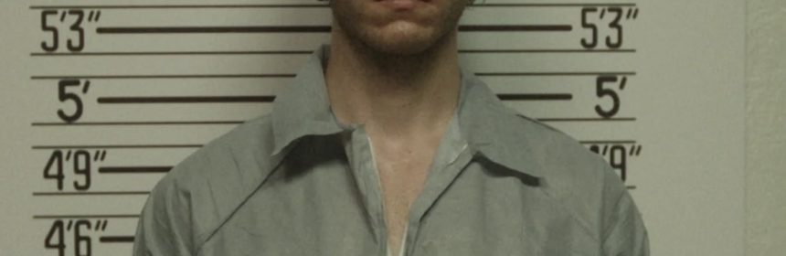 man with glasses standing in front of height measurment