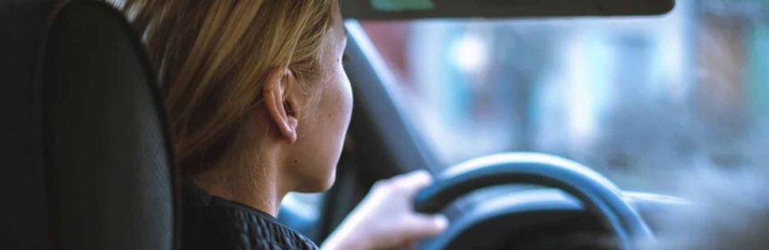 back of lady in car driving with hands on the wheel