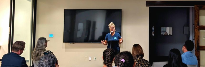 lady in blue shirt standing while people in chairs sit and watch her