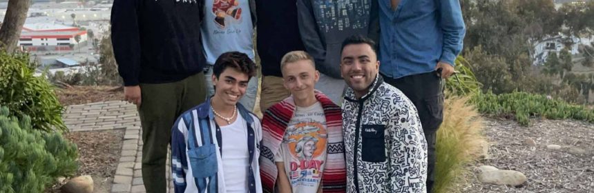 two rows of eight people standing outside under a tree smiling