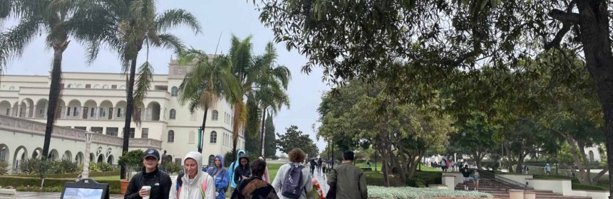 students in coats walking in the rain on a wet sidewalk with trees above them