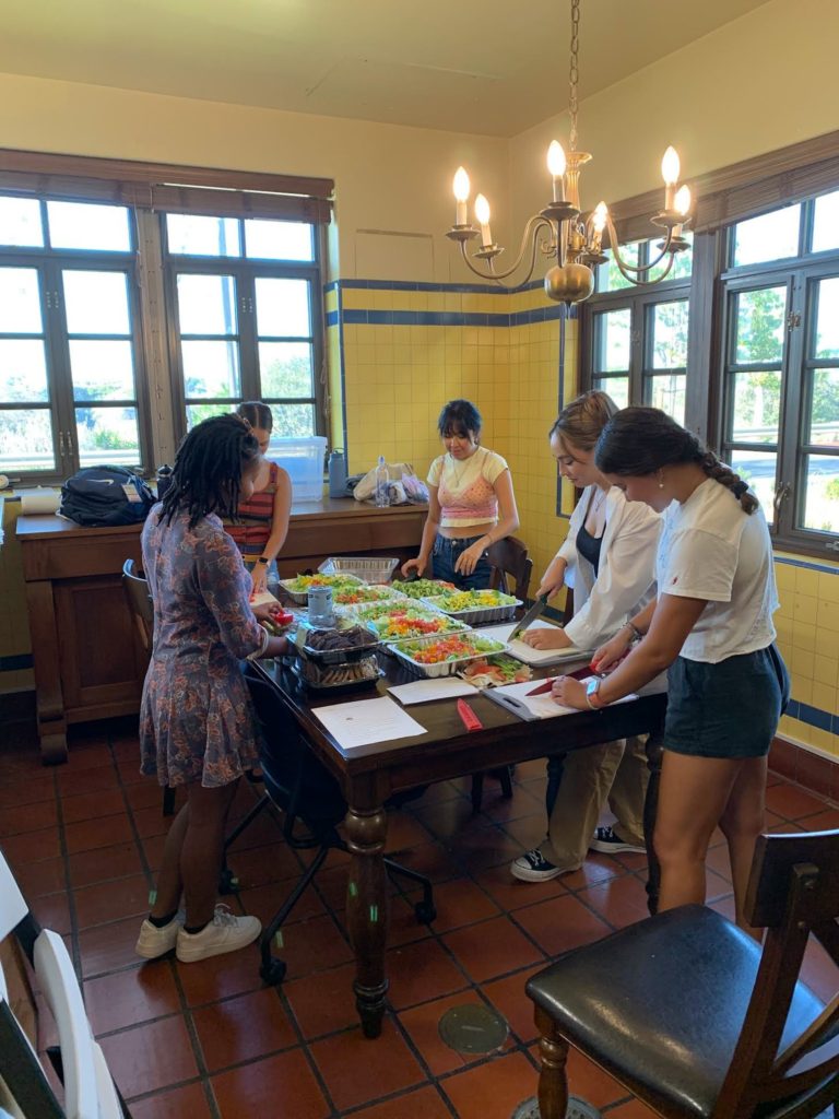 five people standing around a table with trays of food on it.