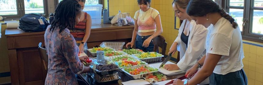 five people standing around a table with trays of food on it.