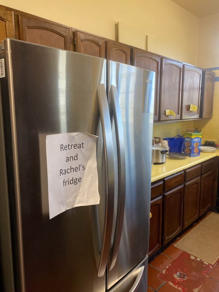 a silver fridge with a white sheet of paper taped on reading "retreat and rachel's fridge"